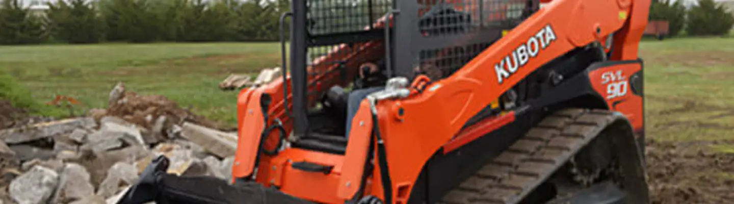 A truck loader actively digging and moving rocks at a construction site, with safety barriers visible in the background.