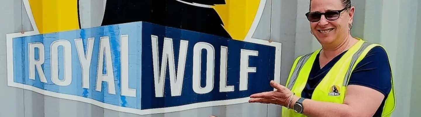 Woman standing and smiling in front of a company logo, representing professionalism and company pride.