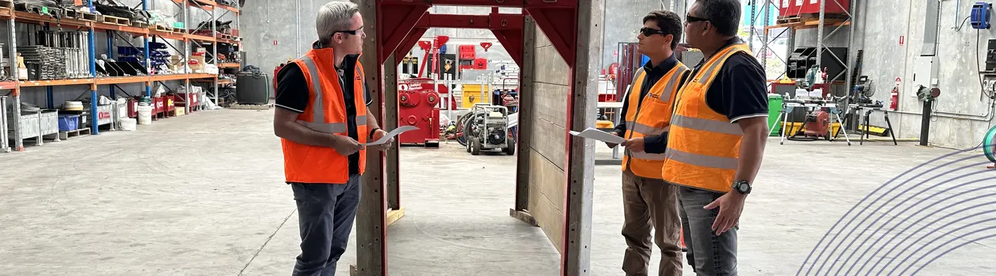 Three engineers talking to each other and standing in front of an aluminium shoring box.