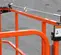 Side view of orange rental lift with safety rail and warning label sitting on concrete surface.