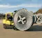 Side view of a yellow warehouse forklift carrying a large grey reel with an operator in an open cabin at an outdoor jobsite.