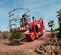 Front angled view of red boom lift with platform and guardrails, on uneven outdoor terrain.