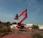 Rear view of a red atrium lift with extended arm, stabilizers and basket with an operator using lift in outdoor work zone.