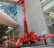 Rear view of a red atrium lift with extended arm and stabilizers, operator using lift indoors near glass windows.