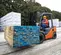 Front angled view of an orange and grey warehouse forklift lifting lumber on an outdoor construction site.