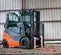 Front angled view of orange and grey Toyota warehouse forklift with a mast, orange forks and enclosed cabin in a warehouse.