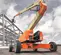 Rear view of an orange and beige Genie boom lift with extended arm in use on an outdoor construction site.