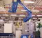 Rear view of blue Genie Boom lift with extended arm and basket, in an indoor warehouse, with operator on platform.