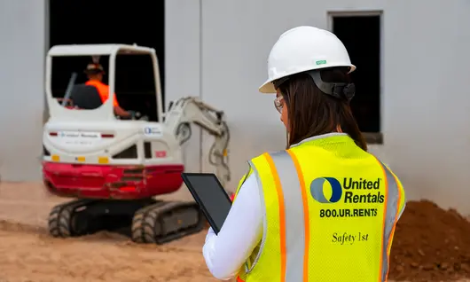woman on jobsite holding ipad next to skid steer