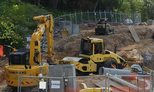 Different types of construction equipment in use at a site, supporting tasks like excavation, lifting, and barrier installation.