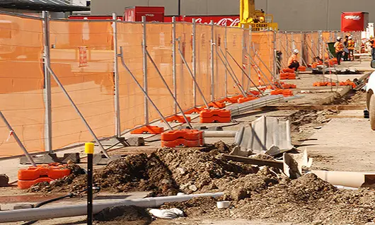 Safety fencing with braces and netting surrounding a construction worksite to prevent debris and unauthorized access.
