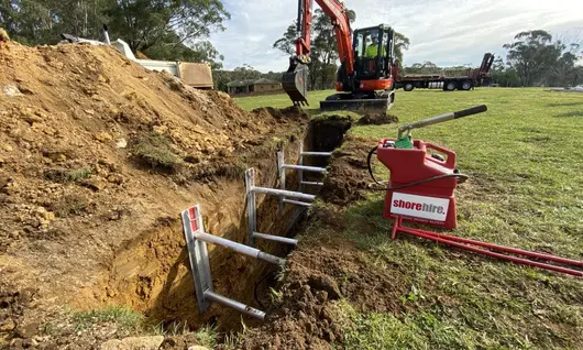 Construction site with a small panel placed inside a digging hole, surrounded by safety barriers and warning signs.