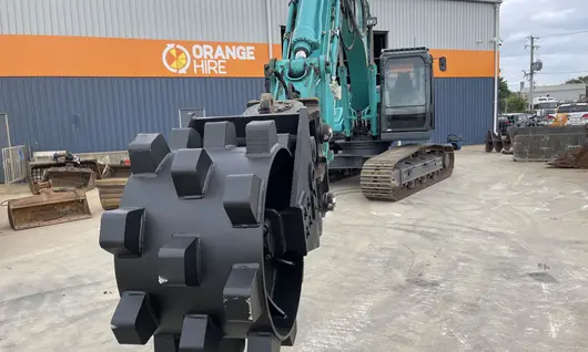 Compaction wheel attached to construction equipment, used for securing soil around newly installed safety barriers.