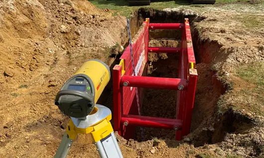 Pipe laser operating in trench with protective blue shield for pipe alignment             