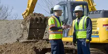two men in hard hats on construction site with excavator 