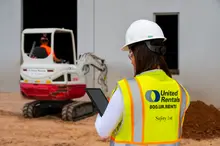 woman on jobsite holding ipad next to skid steer