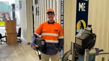 Person in hi-vis holding a welding helmet standing in front of a container.