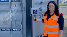 A woman in a hi-vis vest holding the door of a shipping container open.